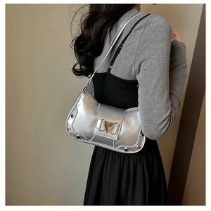 Detail of silver metallic underarm bag featuring a heart-shaped buckle and rivet accents