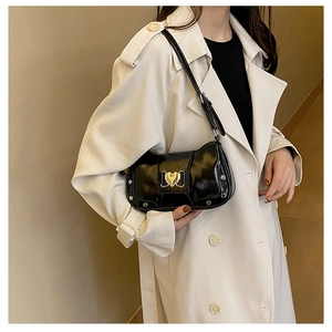 Detail of black glossy underarm bag with gold heart clasp and silver rivets
