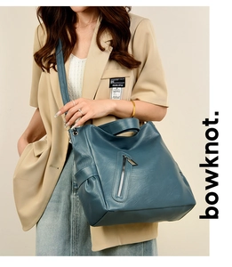Detail of dark blue leather tote bag showing vertical zipper and soft texture on model