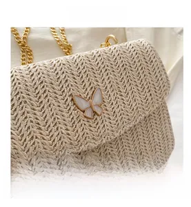 Detail view of beige woven straw shoulder bag featuring a golden chain and butterfly clasp