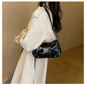 Detail of black glossy shoulder bag with silver heart buckle on a beige trench coat