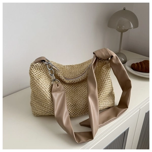 Close-up of beige woven tote bag featuring a brown strap with knot and silver chain link