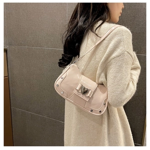 Detail of pink glossy shoulder bag with silver heart buckle and rivets on sweater