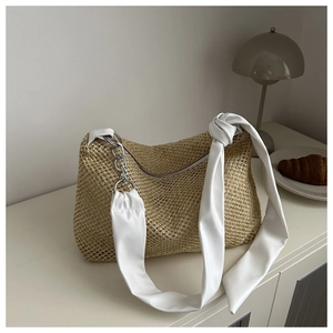 Close-up of woven straw tote bag with unique knot strap and silver chain details