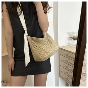 Detail of hollow woven straw tote bag with wide fabric strap and knot decoration