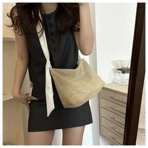 Detail of hand-woven straw tote bag featuring a decorative knotted white wide shoulder strap