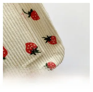Vue macro du sac cabas en velours côtelé montrant la broderie fraise et le tissu