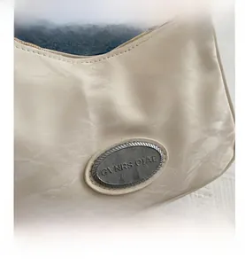 Close-up of creamy white shoulder bag featuring wrinkled texture and oval metal plate