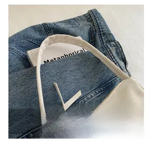 Detailed view of a white minimalist underarm bag with slim handles on denim background