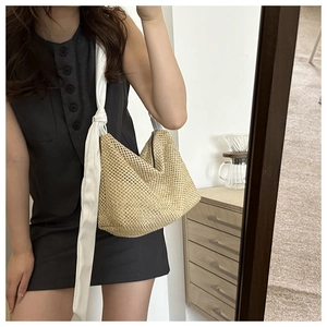 Detail of hollow-out woven straw tote with wide white fabric knotted shoulder strap