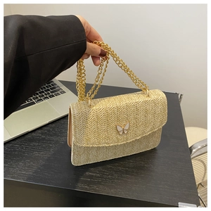 Detail of straw woven bag featuring a golden chain strap and white butterfly buckle