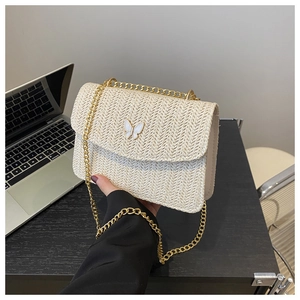 Detail of a beige straw woven crossbody bag featuring a decorative white butterfly clasp