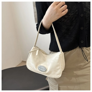 Close-up of cream pleated shoulder bag with metallic oval logo worn on model shoulder