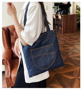 Detail of dark blue denim tote bag featuring reinforced stitching and large front pocket