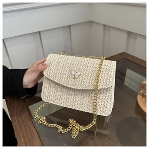 Close-up of woven straw bag featuring gold butterfly buckle and metal chain strap