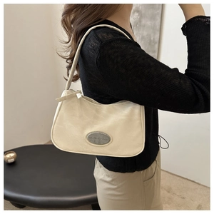 Detail of cream underarm bag with pleated texture and oval metal brand emblem