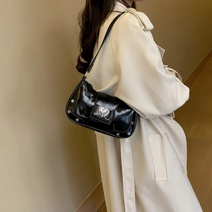 Glossy black Y2K underarm bag with silver heart buckle and rivets shown on a beige trench coat