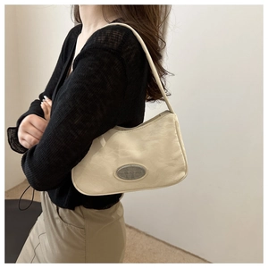 Close-up of beige underarm bag with pleated texture and silver oval metal plate detail