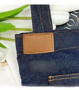 Detail of blue denim tote bag featuring orange contrast stitching and leather patch