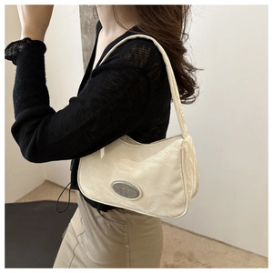 Model wearing a cream pleated underarm bag with a stylish silver metal nameplate