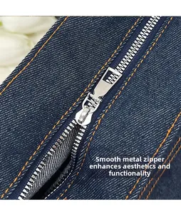 Close-up of polished silver metal zipper and orange contrast stitching on blue denim bag