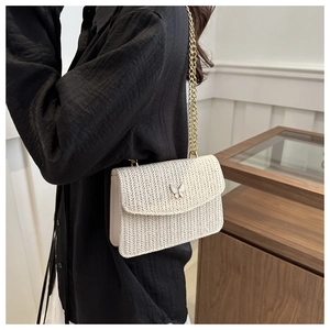 Detail of cream woven crossbody bag featuring golden butterfly clasp and chain strap