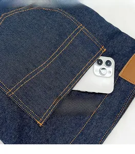 Macro view of large storage pocket on denim tote bag with durable orange contrast stitching