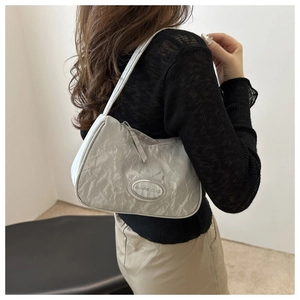 Detail of silver underarm bag with metallic pleated texture worn by a model