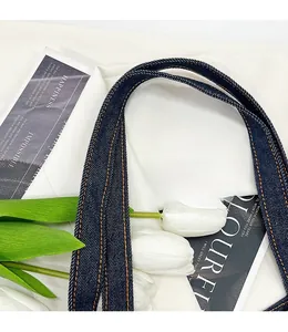 Detail of blue denim tote bag handle featuring reinforced double yellow stitching