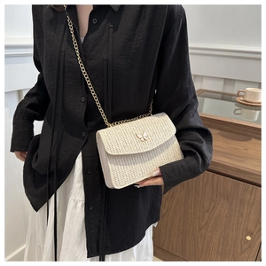 Detail of cream straw crossbody bag featuring a golden butterfly clasp and chain strap