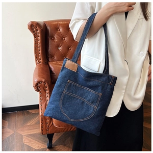 Detail of deep blue denim tote bag with contrast stitching and leather patch on handle