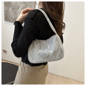 Close-up of metallic silver pleated underarm bag with an oval metal logo plate