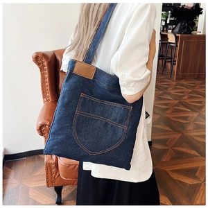Detail view of large denim tote bag featuring brown leather patch and orange contrast stitching