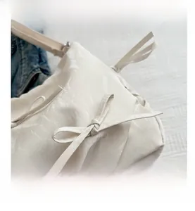Detail shot of beige pleated PU material bag with decorative bow and textured shoulder strap