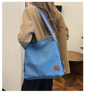 Detail of adjustable wide shoulder strap on blue denim crossbody bag with leather logo tag