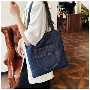 Close-up of dark blue denim tote bag featuring retro orange stitching and a large front pocket