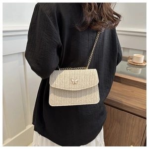 Detail of beige straw crossbody bag with golden butterfly charm and woven chain strap