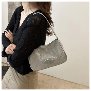 Detail of silver pleated underarm bag showing mirror texture and embossed oval logo