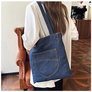 Detail of dark blue denim tote bag featuring orange contrast stitching and front pocket