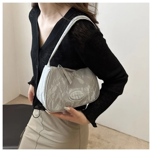 Detail of silver-grey pleated texture underarm bag with oval metal logo plate