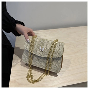 Detailed view of woven straw bag with white butterfly hardware and gold chain strap