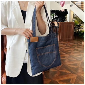 Detail of dark blue denim tote bag with orange stitching and faux leather patch
