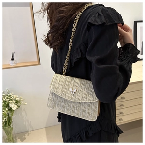 Detail view of straw woven crossbody bag with butterfly buckle and gold chain strap