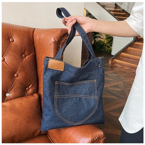 Detail of vintage blue denim tote bag with contrast stitching and pocket on leather sofa