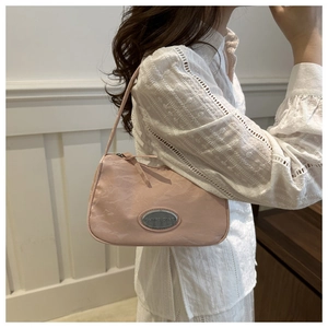 Close-up of pink underarm bag with silver logo plate and subtle wrinkled texture fabric