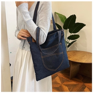 Detail of blue denim tote bag with orange contrast stitching and front pocket design