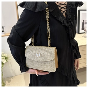 Close-up of woven straw shoulder bag featuring a white butterfly buckle and gold chain strap