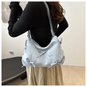 Detail of light blue pleated nylon shoulder bag with bow accents worn by a model