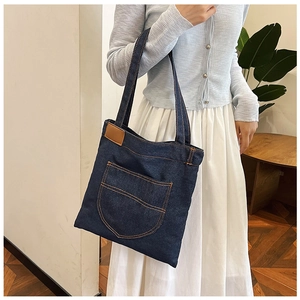 Detail of dark blue denim tote bag with orange stitching and brown leather patch