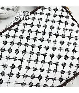 Close-up of white crossbody bag featuring black clover patterns and brown leather piping